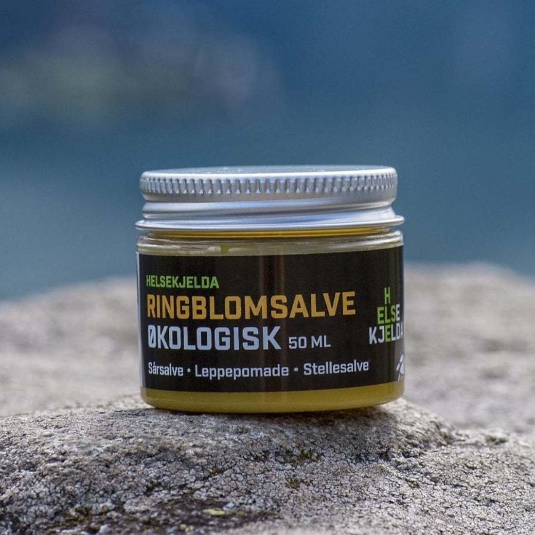 Helsekjelda ringblomsalve 50 ml i glasskrukke med sølvlokk på en stein