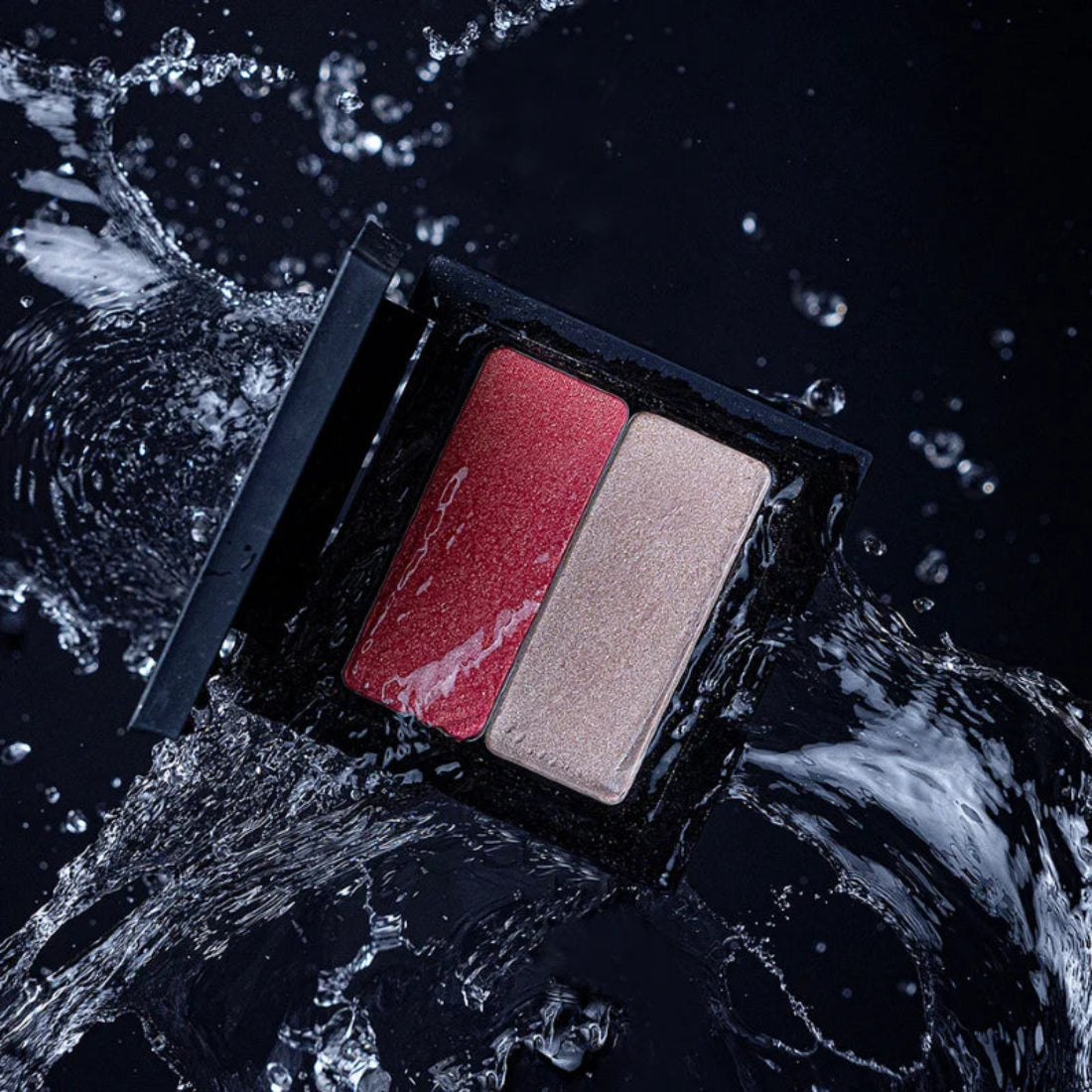 Åpen svart sminkepalett med rosa blush og lys skimrende highlighter, omgitt av vannsprut mot mørk bakgrunn