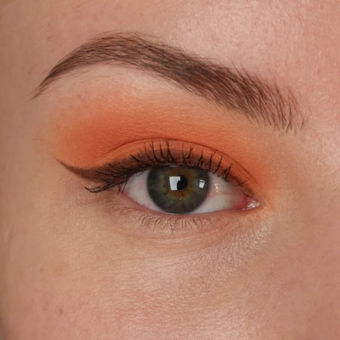 Nærbilde av et øye med ferskenoransje øyenskygge og mørk eyeliner med vinge