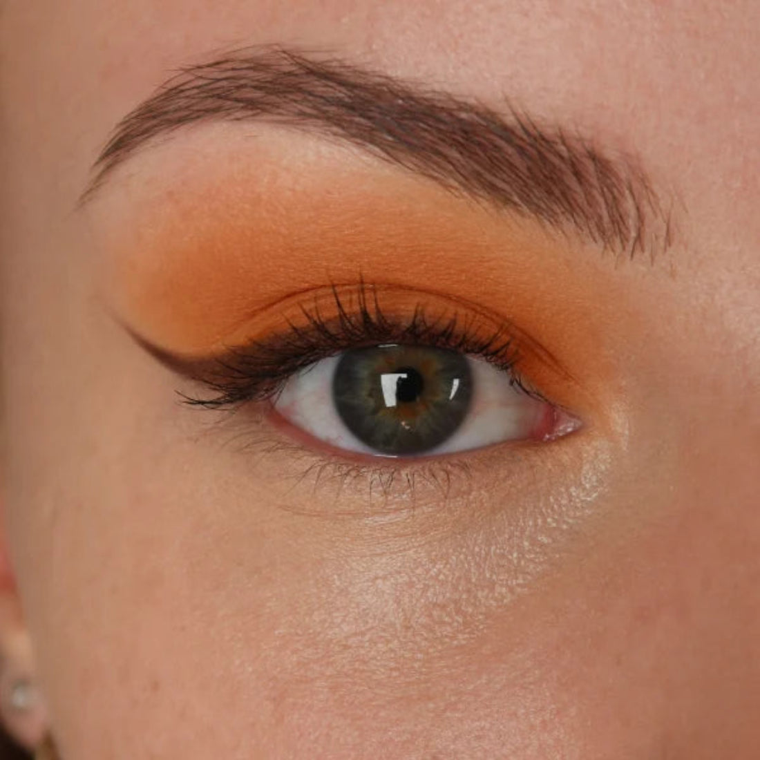 Nærbilde av et øye med varm oransje øyenskygge og mørk eyeliner med vinge