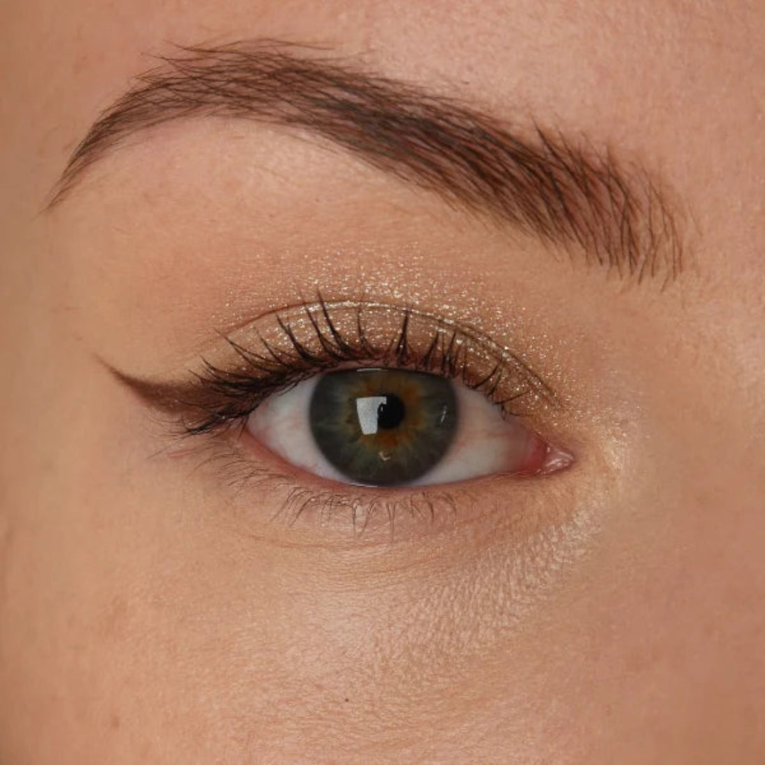 Nærbilde av et øye med lys skimrende øyenskygge og mørk eyeliner med vinge