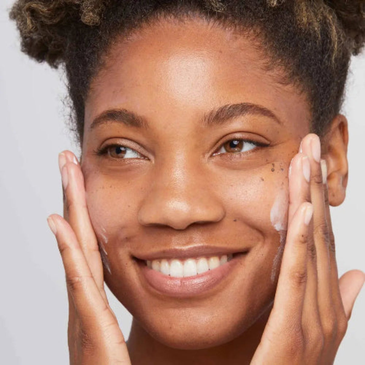 Smilende kvinne som påfører Dermalogica Skin Smoothing Cream på kinn med fingertuppene – bestselgende fuktighetskrem for alle hudtyper
