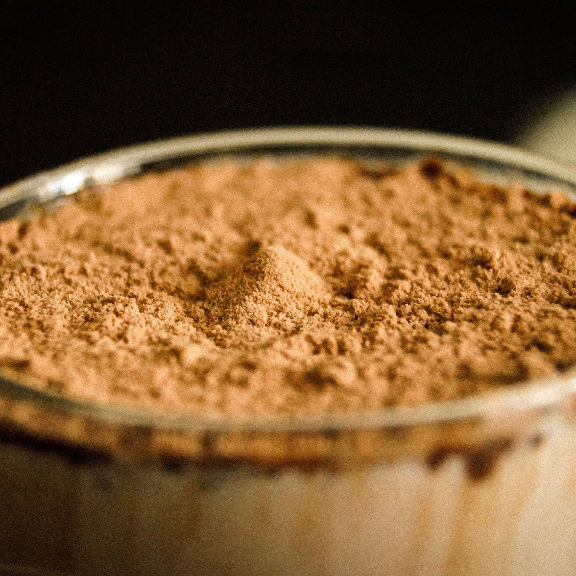 Nærbilde av fint kakaopulver i glasskål mot mørk bakgrunn – kakao er smaksingrediensen i Herba Plus Glucoboss Choco lavkarbo næringspulver med glucomannan og kanel, 400 g