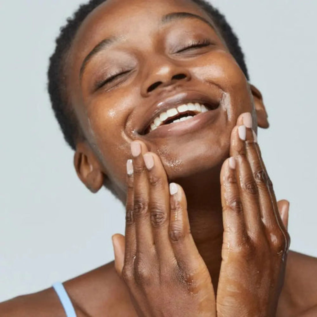 Smilende kvinne som masserer Dermalogica PreCleanse inn i huden – oljebasert prereins som smelter bort smuss, sminke og solkrem raskt og effektivt