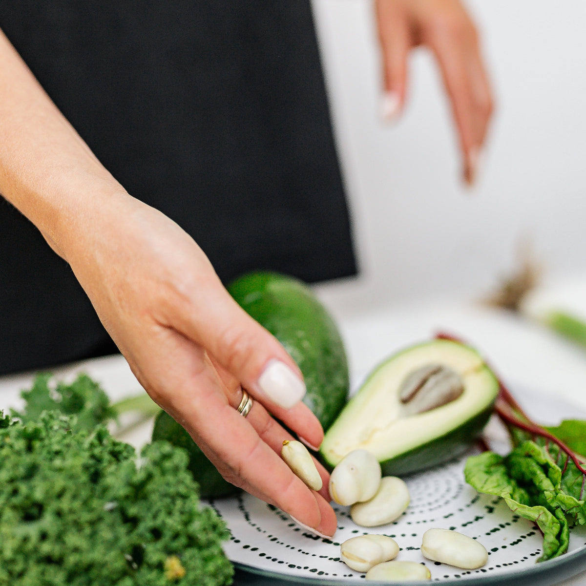 Kvinnehånd som arrangerer avokado, cashewnøtter og grønnkål på tallerken – grønne grønnsaker og nøtter er naturlige kilder til krom og sink, nøkkelmineralene i Herba Plus Glucoboss Balance