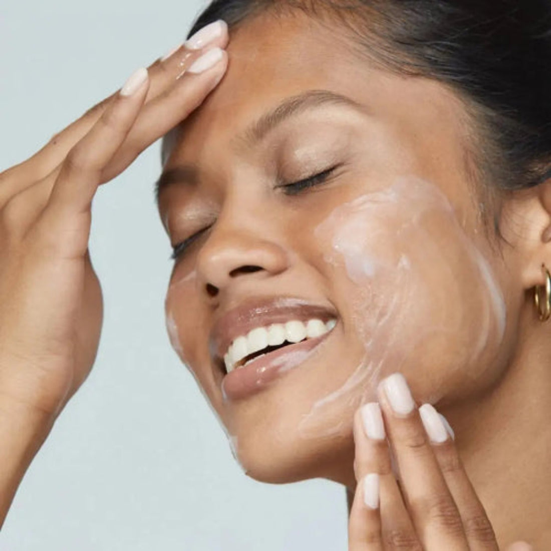  Smilende kvinne som påfører Dermalogica Intensive Moisture Balance på kinn og panne – fuktighetskrem for tørr og dehydrert hud