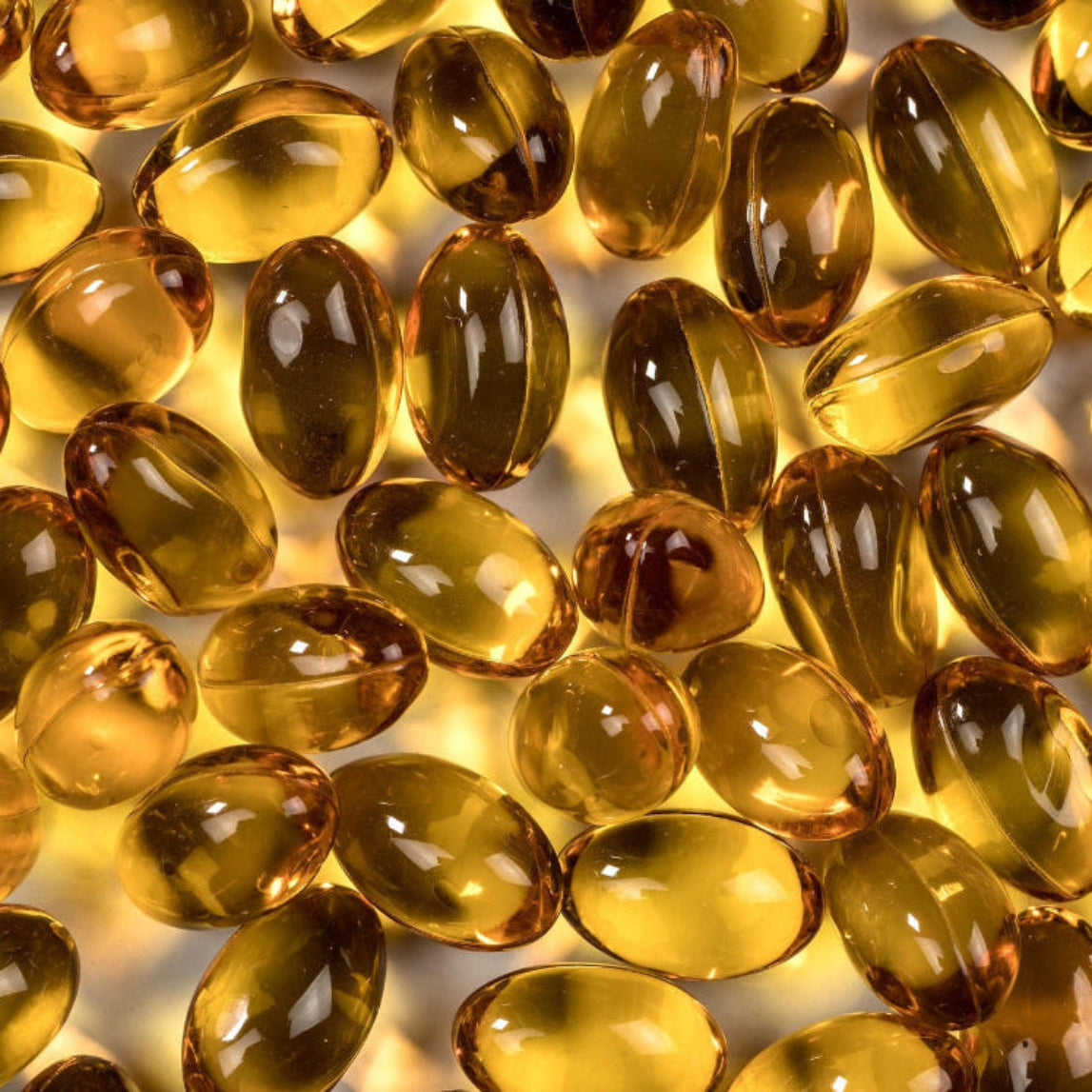 Nærbilde av gule og brune omega-3 gelkapsler i sterkt lys – krillolje og fiskeolje i kapselform slik det finnes i Herba Plus Krill Plus for daglig inntak av essensielle fettsyrer
