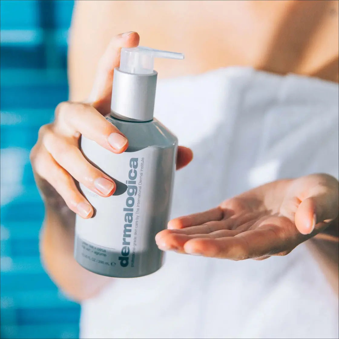 Kvinne i hvitt badehåndkle som pumper Dermalogica Body Hydrating Cream i hånden – daglig kroppsfukt for glatt og glødende hud