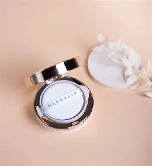  Nanoasia Cushion Foundation SPF 50, sølv kompaktboks med speiløvre og hvit puff, åpen på beige overflate med hvite blomster, koreansk cushion med peptider og edelstenekstrakter, vektløs tekstur med refill-mulighet