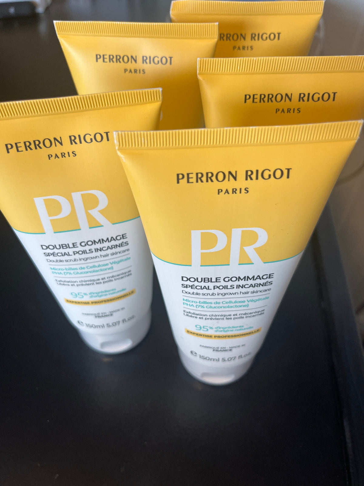 Fem gule og hvite tuber med Perron Rigot Double Scrub kroppsskrubb på mørk flate