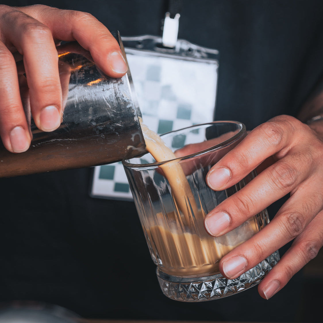 Hender som heller en sjokoladefarget drikke fra shakerbeger i krystallglass – illustrerer tilberedning av Herba Plus Glucoboss Choco lavkarbo sjokoladeshake med glucomannan
