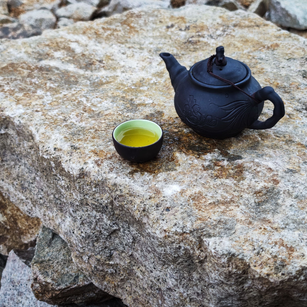 Tradisjonell svart leiretekannen og kopp med grønn te på steinblokk – grønn te er en klassisk urt i asiatisk urtetradisjon, nøkkelingrediens i Herba Plus Grønn Te urtepulver